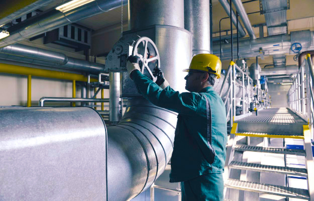 Mann mit gelbem Helm dreht an Rad im infra Heizkraftwerk